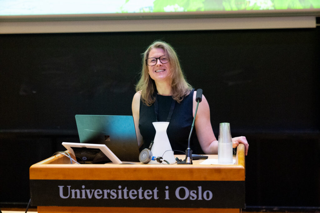 Dr. Courtney Bell stands behind a lectern smiling while presenting at the QUINT Conference in June 2024.